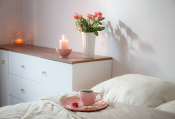 Fototapeta na wymiar pink cup of coffee on bed with flowers in vase in white bedroom
