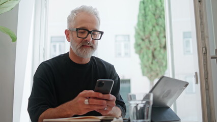 Smiling senior texting smartphone in cafe closeup. Successful bearded man browse