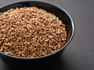 Buckwheat in a black bowl on a black surface. Closeup.