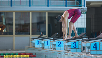 Sportswoman, a professional swimmer at the start of the swimming race, beginning drive from the block, flighting and entering into the pool water