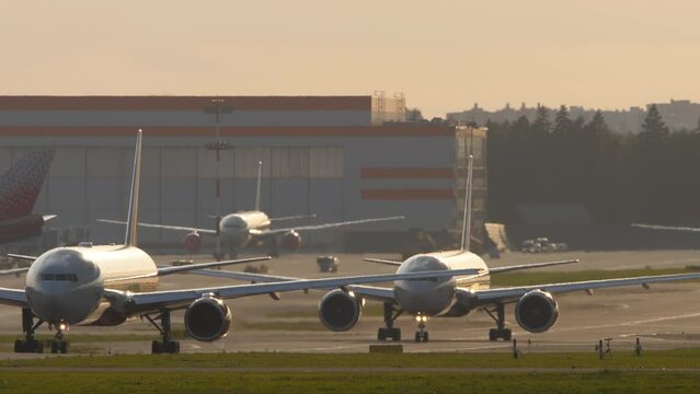 Planes on the taxiway one after another in backlight. Airfield, queue of jet planes, aviation. Travel concept
