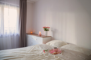 Fototapeta na wymiar pink cup of coffee on bed with flowers in vase in white bedroom