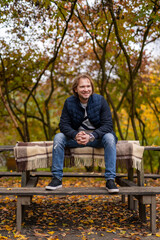 A Man Sitting on a Bench in a Park. In this photo, a man is peacefully seated on a bench in a serene park, enjoying the tranquility and beauty of nature.