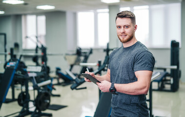 Man Standing in Gym Holding Tablet, Fitness Tracking Technology in Action. A man is captured in...