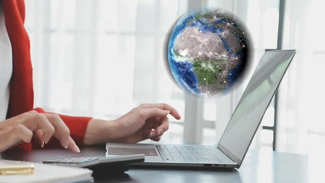 Mujer de negocios observa el globo terr&aacute;queo girando con puntos que se van conectando unos con otros, mientras trabaja en su laptop, hace c&aacute;lculos y toma nota.