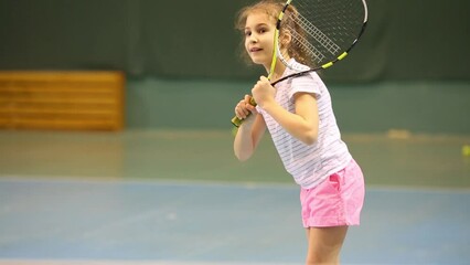 Happy girl learns to beat off balls during tennis training