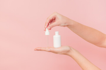 White tube with pipette with serum lotion or essential oil (hyaluronic acid and collagen) in hands on pink background. Skin care cosmetics concept, beauty flyer