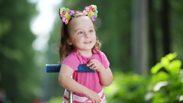 Little cute girl poses near scooter in summer park