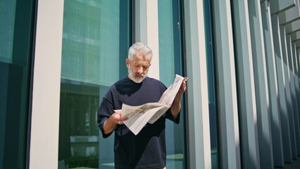 Mature businessman read newspaper on city street. Focused senior rest outdoors