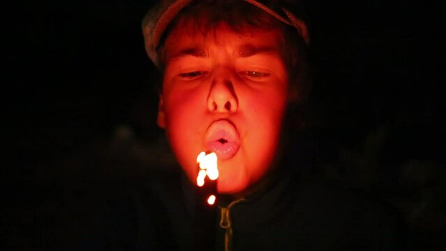 Face of boy blowing at smoldering branch at dark night