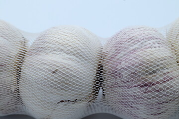 Whole garlic in transparent white net. Close up and isolated.