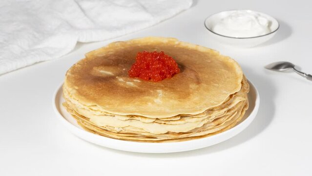 Stack of russian thin pancakes blini with red caviar on white table. Stop motion animation of stack of Russian blinis, thin pancakes or crepe. High quality 4k footage