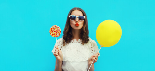 Portrait of happy young woman with yellow balloon on blue studio background - obrazy, fototapety, plakaty