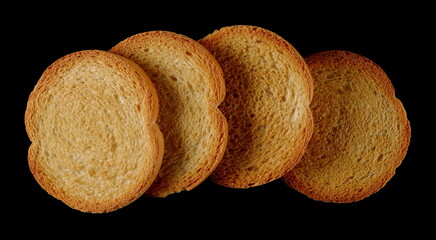 Round bread rusks pile, whole wheat toast slices isolated on black background, top view