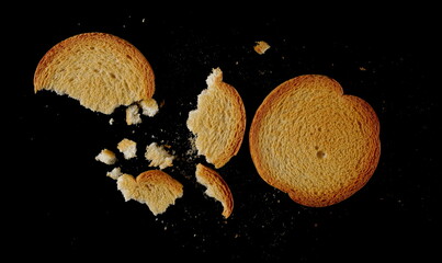 Broken round bread rusks with crumbs, whole wheat toast slices isolated on black background, top view