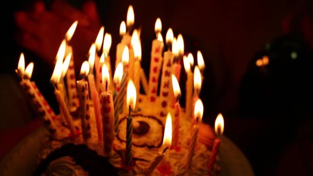 Cake with burning candles in dark close up and people around.