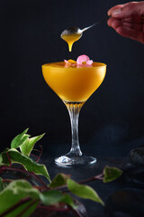 Mango Margarita in a glass on a black background. Alcoholic cocktail based on mango pulp. The cocktail is decorated with a pink flower.Vertical photo.