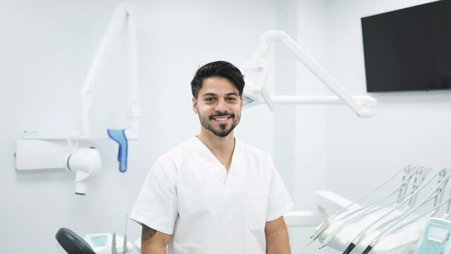 Portrait of a male dentist looking at the camera removing his surgical mask in a modern dental clinic. Cheerful male dentist taking off his mask after a dental operation in the modern surgery.