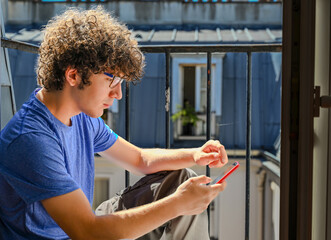 Nice shot of a young Caucasian man intent on consulting his cell phone. He is sitting on the edge of an attic window, the natural light illuminates his face and hair.
