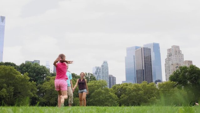 Mother and two children run on grassy lawn, rear low angle view.