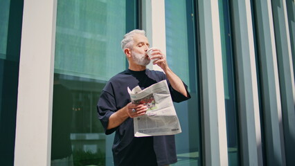 Aged businessman drinking coffee at downtown. Thoughtful senior read newspaper