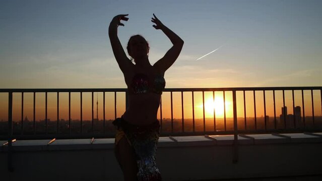 Woman expressive dancing in Asian style at sunset on roof.