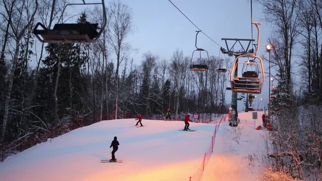 Ropeway above track with skiers at evening in ski resort