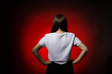 A woman stands with her back to the camera, hands on hips, against a red background, exuding...