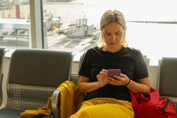Airport terminal. Woman waiting for flight using smartphone. Girl with cell phone in airport...