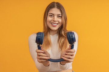 A woman smiling holding blue headphones towards camera