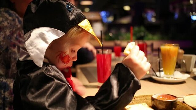 Cute boy in costume with spider painted on cheek eats pancakes
