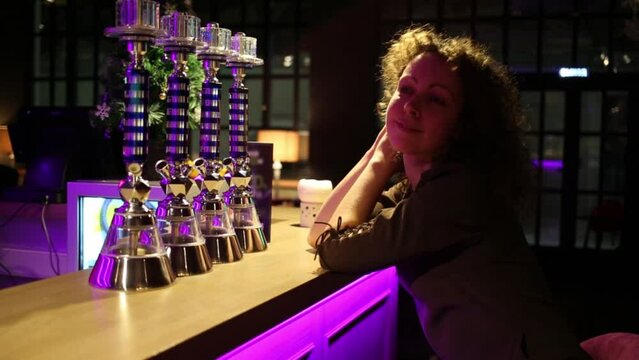 Beautiful woman with curly hair sitting at bar with neon lights