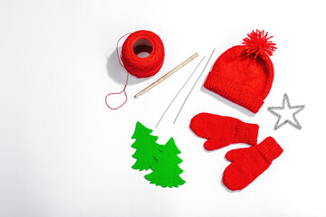Creative handmade winter flat lay. Red knitted mittens and hat, traditional decor, yarn and tools