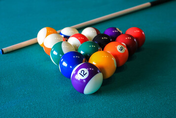 Multi colored billiard balls in the form of a triangle with numbers and cue ball on a pool table....