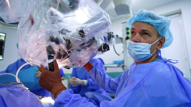 Male neurosurgeon adjusting microscope to the work at operation. Technological equipment is prepared to usage at procedure.
