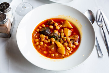 Spanish cuisine, chickpea shepherd soup with potatoes and sausages on a ceramic plate in restaurant