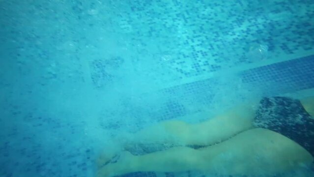 Woman dives into pure water of indoor pool and boy looks at she