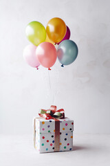 Colorful balloons tied to a gift box with a bow on a white background.