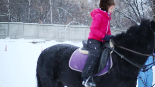 Girl rides on black horse and smiles during snowfall at winter day