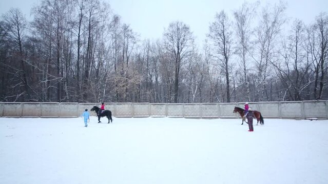 Two girls ride on horses with instructors during snowfall