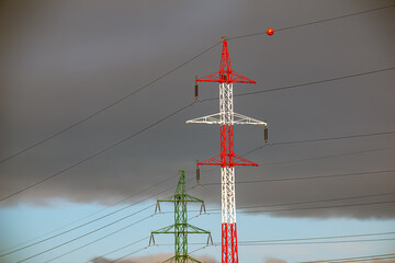 High voltage towers with electrical wires on dark cloudy sky background.