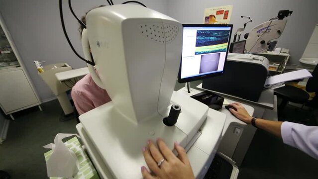 A doctor holds the patient eye exam and watching result on monitor