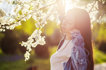 A beautiful young woman with long hair relaxes in a park with flowering trees at sunset in early...