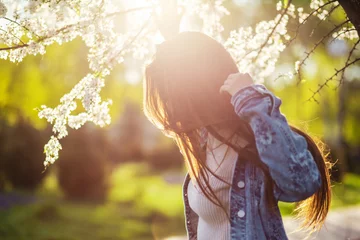 Tuinposter A beautiful young woman with long hair relaxes in a spring park with flowering trees at sunset. © Konstantin Zibert