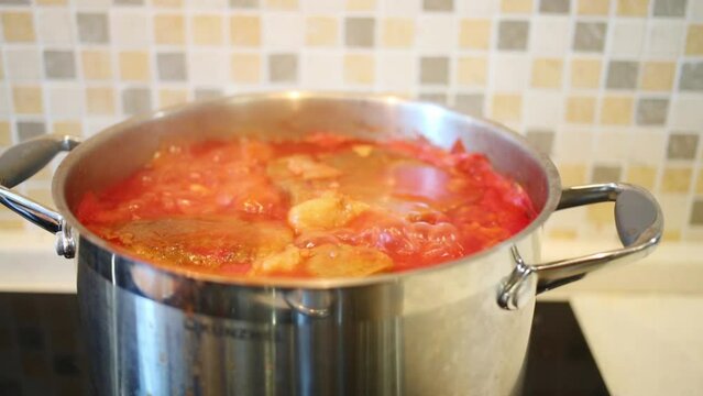 Hot red borsch soup is cooked in metal pan in kitchen