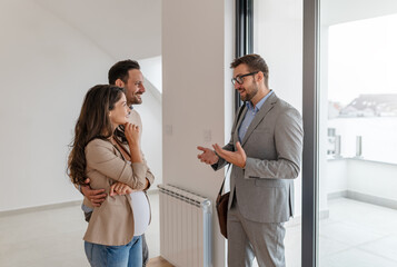 A young, beautiful, cheerful couple expecting a baby, talking with a real-estate agent visiting...