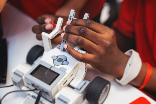 Group of diverse children kids with robotic vehicle model, close-up view on hands, science and engineering lesson in a classroom, making, coding and programming a robot in a school, robotics projects