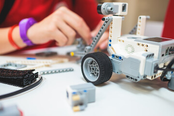 Group of diverse children kids with robotic vehicle model, close-up view on hands, science and engineering lesson in a classroom, making, coding and programming a robot in a school, robotics projects