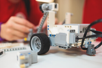 Fototapeta premium Group of diverse children kids with robotic vehicle model, close-up view on hands, science and engineering lesson in a classroom, making, coding and programming a robot in a school, robotics projects