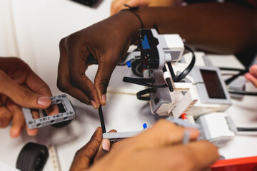 Group of diverse children kids with robotic vehicle model, close-up view on hands, science and engineering lesson in a classroom, making, coding and programming a robot in a school, robotics projects